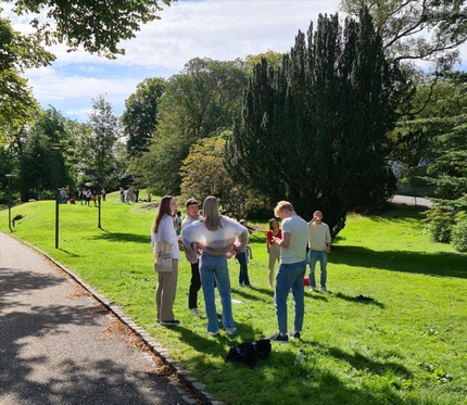 Studenter som blir kjent med hverandre i Nygårdsparken. De står i en sirkel i solen. 