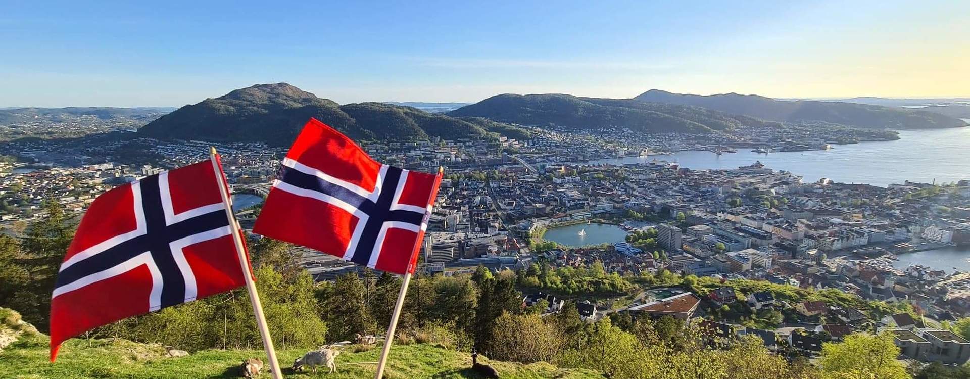 Norske flagg med utsikt over Bergen, fjell og fjord.