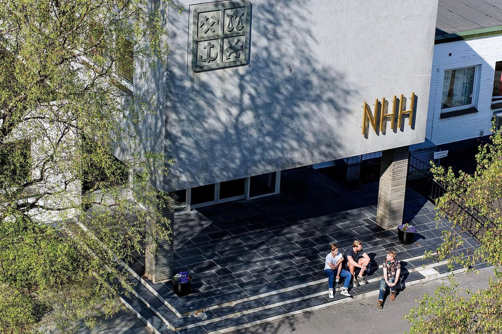 Tre studenter sitter på trappen utenfor hovedinngangen til NHH.