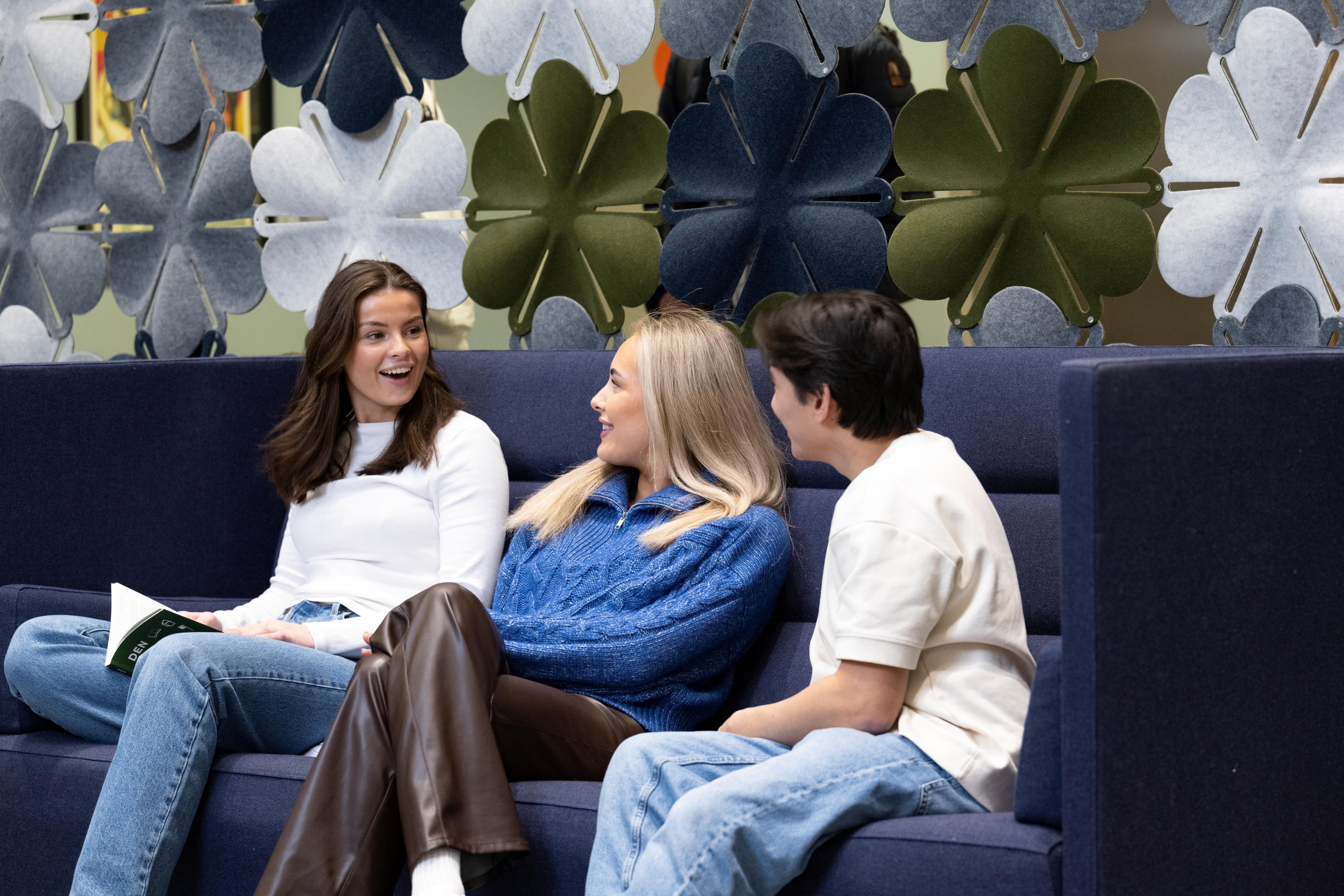 Tre BI-studenter sitter i en sofa og diskuterer.
