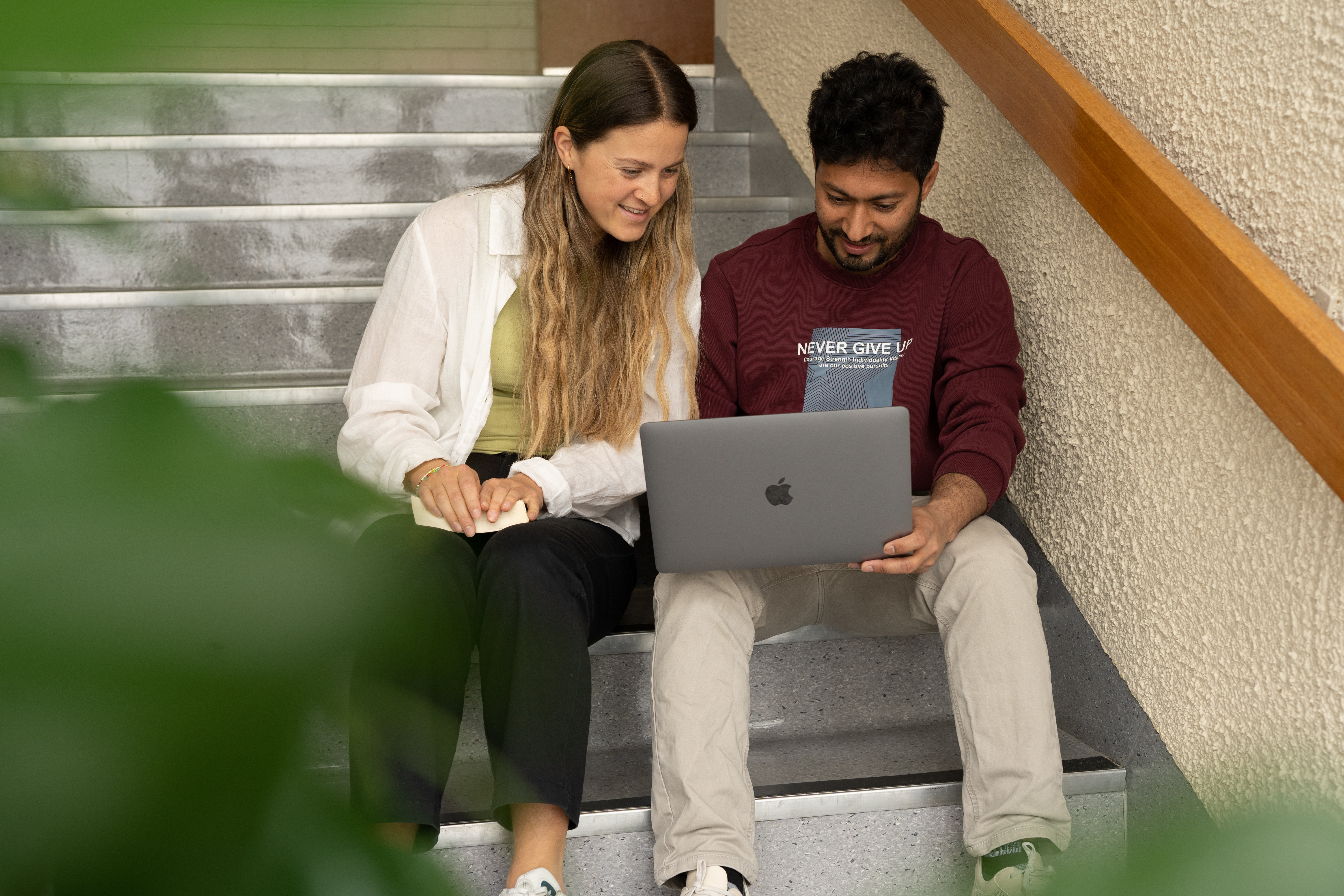 To studenter på NLA Høgskolen samarbeider foran en PC i en trapp