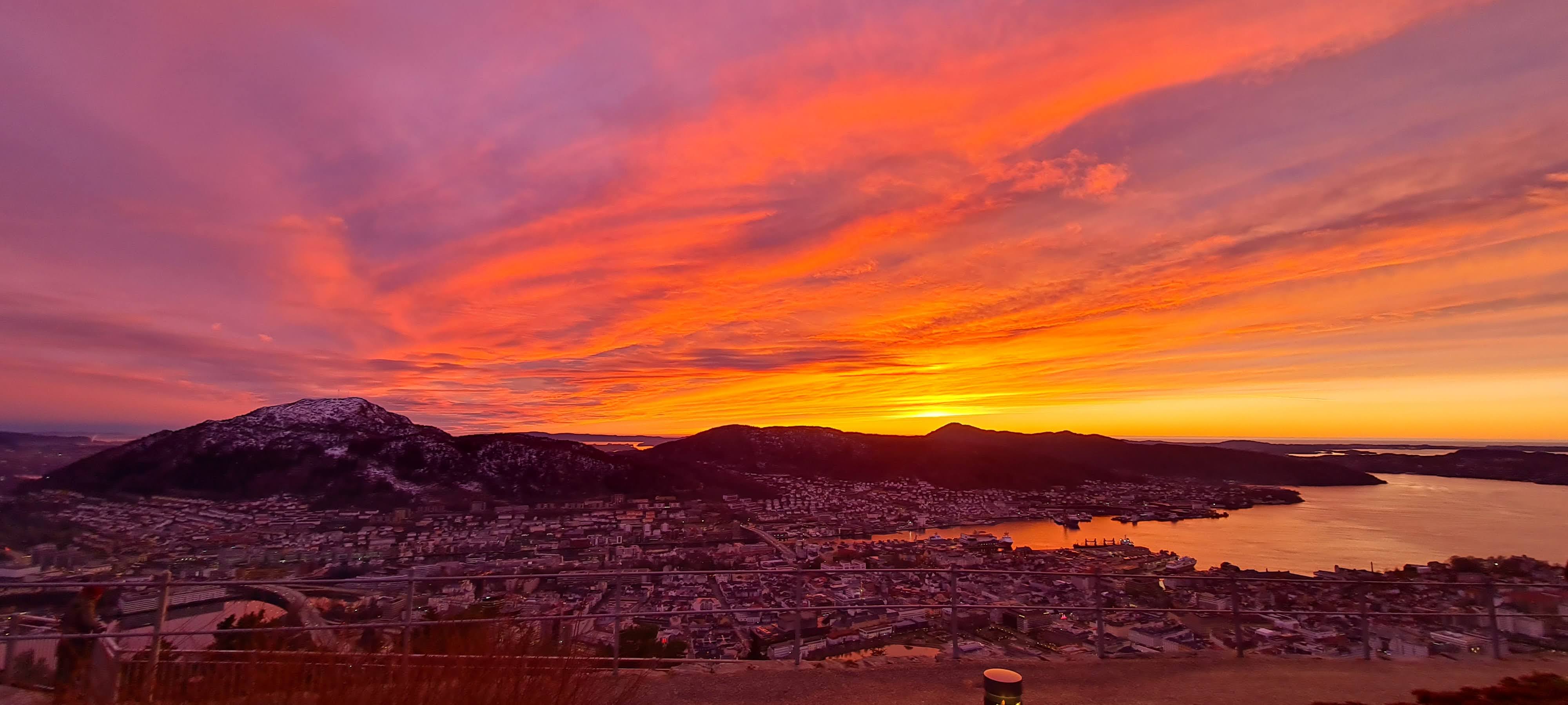 Image of Bergen seen from the top of Fløyen just after the sun has gone down in February. The sky is a blaze for red, yellow and pink tones.