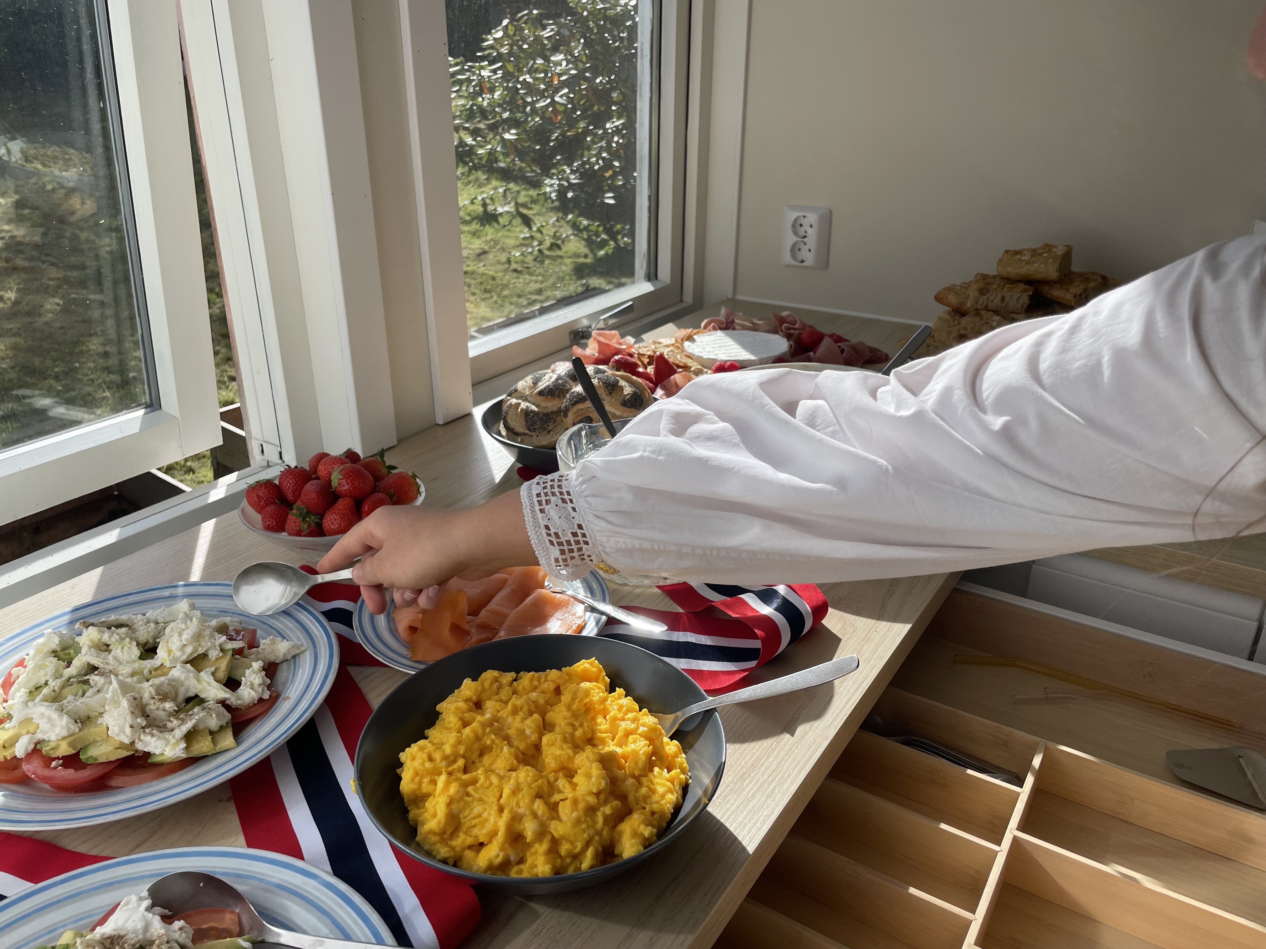 Et bord med ulike 17. mai frokost retter. En som strekker seg over for å servere seg med salat. 