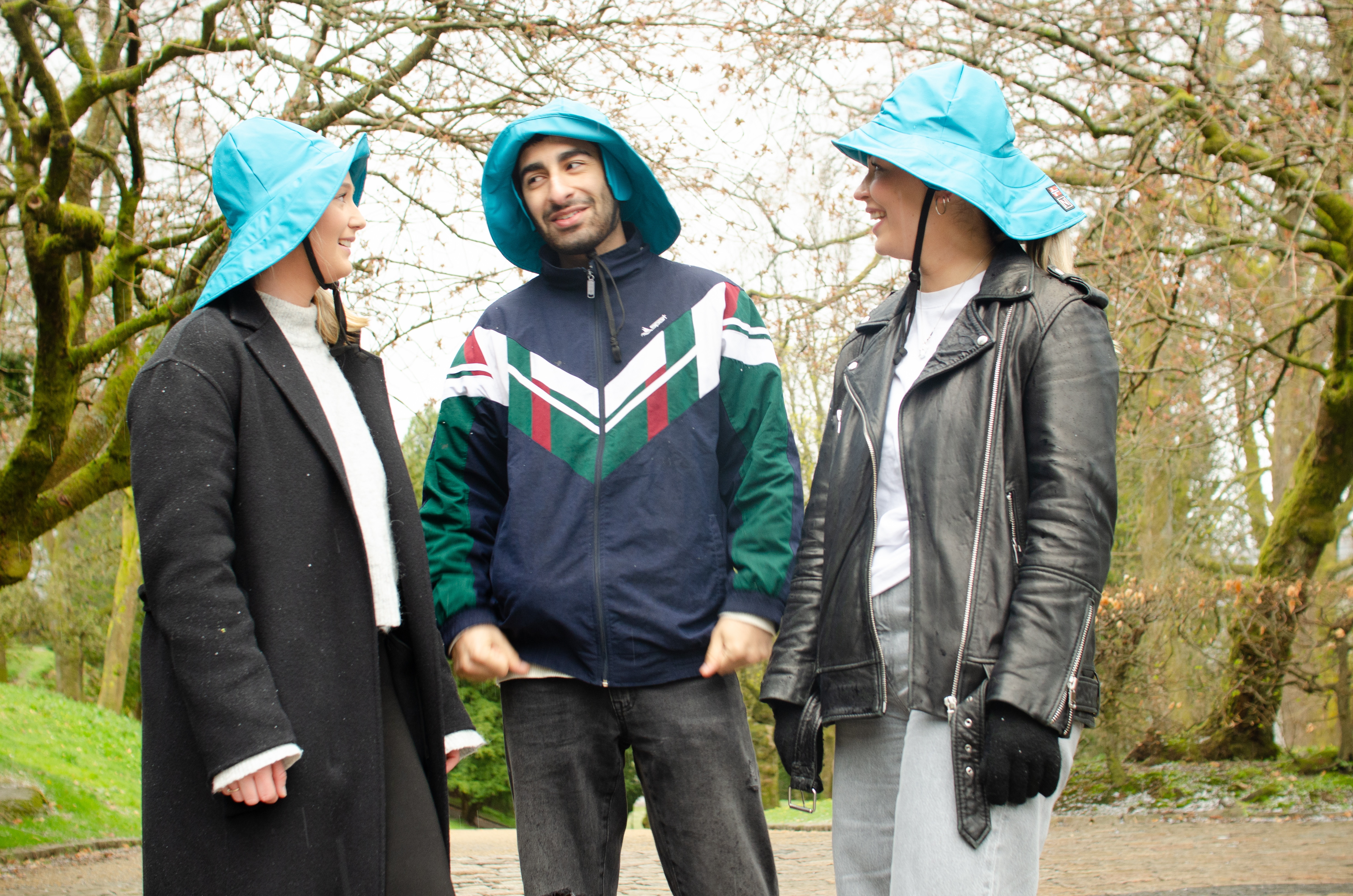 En gjeng med tre studenter som står med hver sin lyseblå sydvest. 