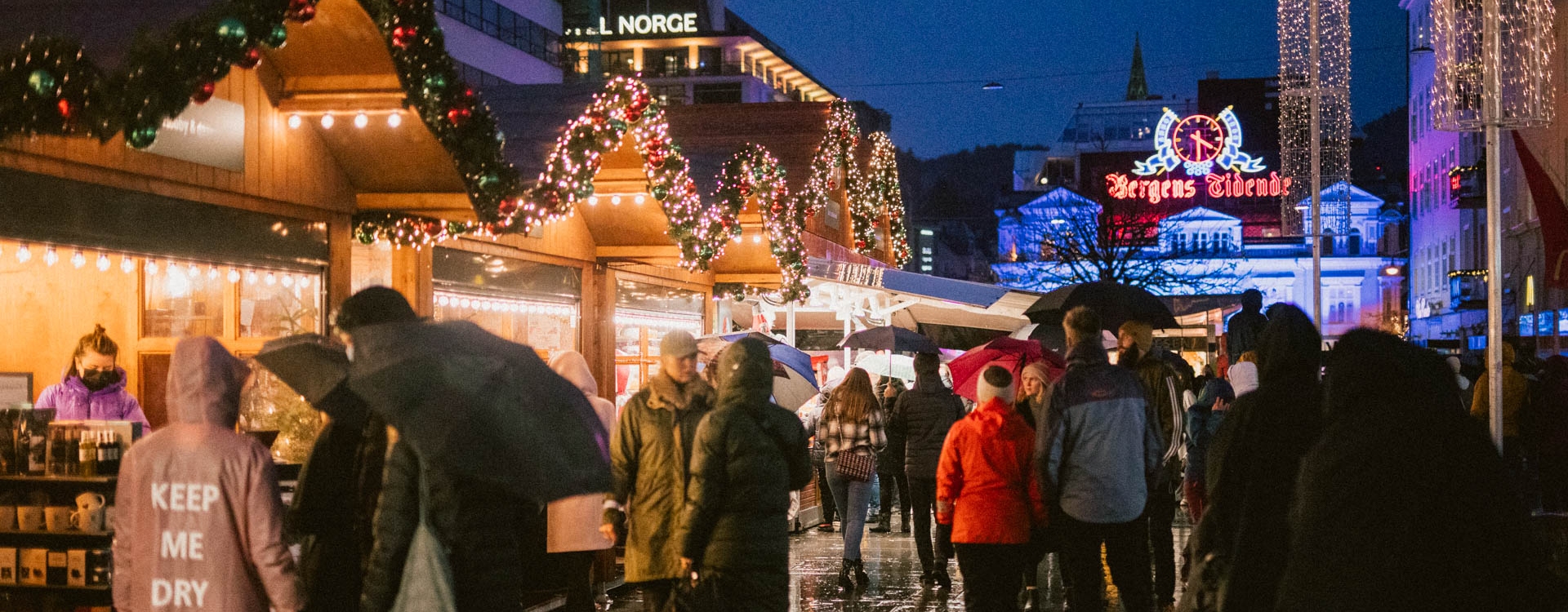 Mange mennesker samlet på julemarked der de ser på produktene som selges, byen er pyntet med julelys.