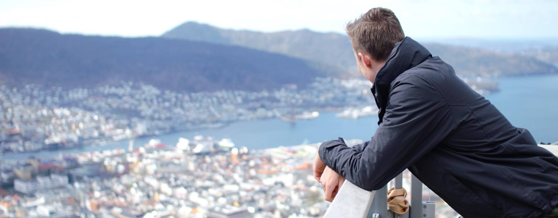 Mann med ryggen til som ser på utsikt over Bergen fra Fløyen.