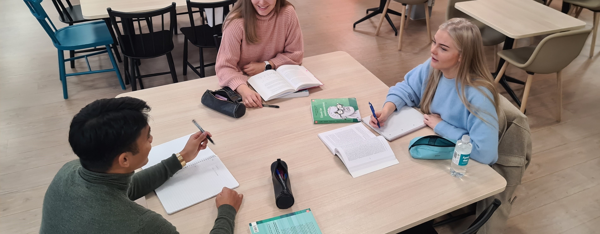 Tre studenter sitter rundt et bord og diskuterer.