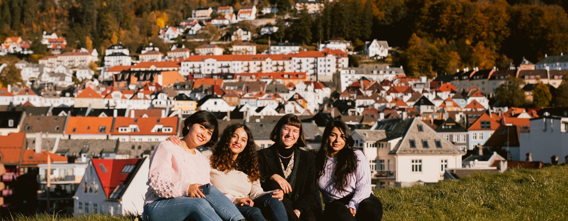 Tre studenter på høsten som sitter i solen langs kaien. 