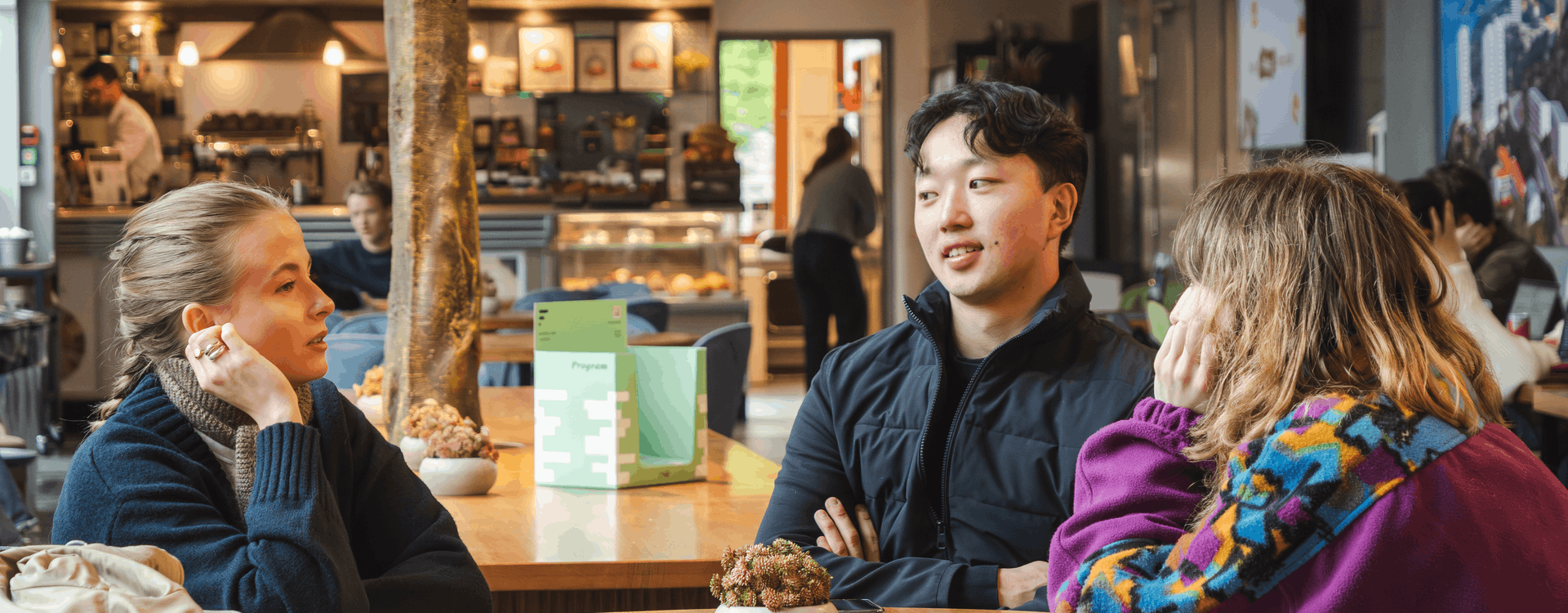 Tre studenter sitter på en kafé og prater.