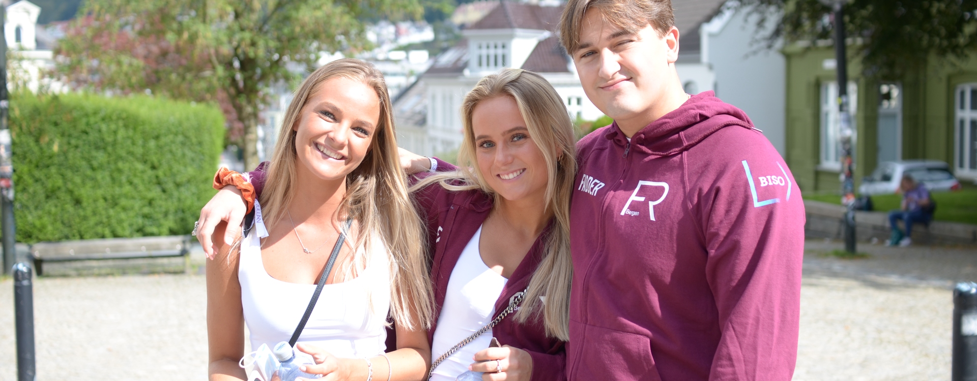 Three students attending the Welcome week, looks in the camera and smiles in sunny UiB campus.