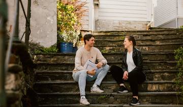 To studenter sitter i en trapp i Bergen og ser på hverandre og smiler. 