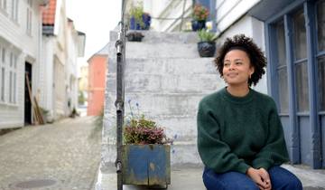 Blid kvinnelig student sitter i en trapp utenfor studentboligen i en gate i Bergen.