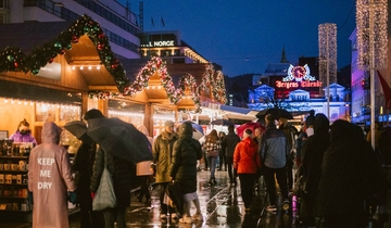 Mange mennesker samlet på julemarked der de ser på produktene som selges, byen er pyntet med julelys.