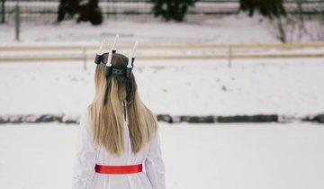 Girl with long blond hair wearing a crown of candles on her head. Seen from behind.