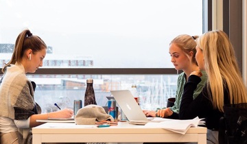 Tre studenter sitter rundt et bord med bøker og PC og leser til eksamen.