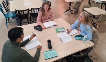 Tre studenter sitter rundt et bord og diskuterer.