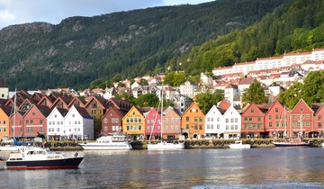 Bryggen i Bergen på våren. Det er sol, grønt og masse båter på vannet foran Bryggen. 