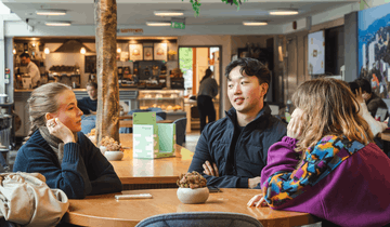 Tre studenter sitter på en kafé og prater.